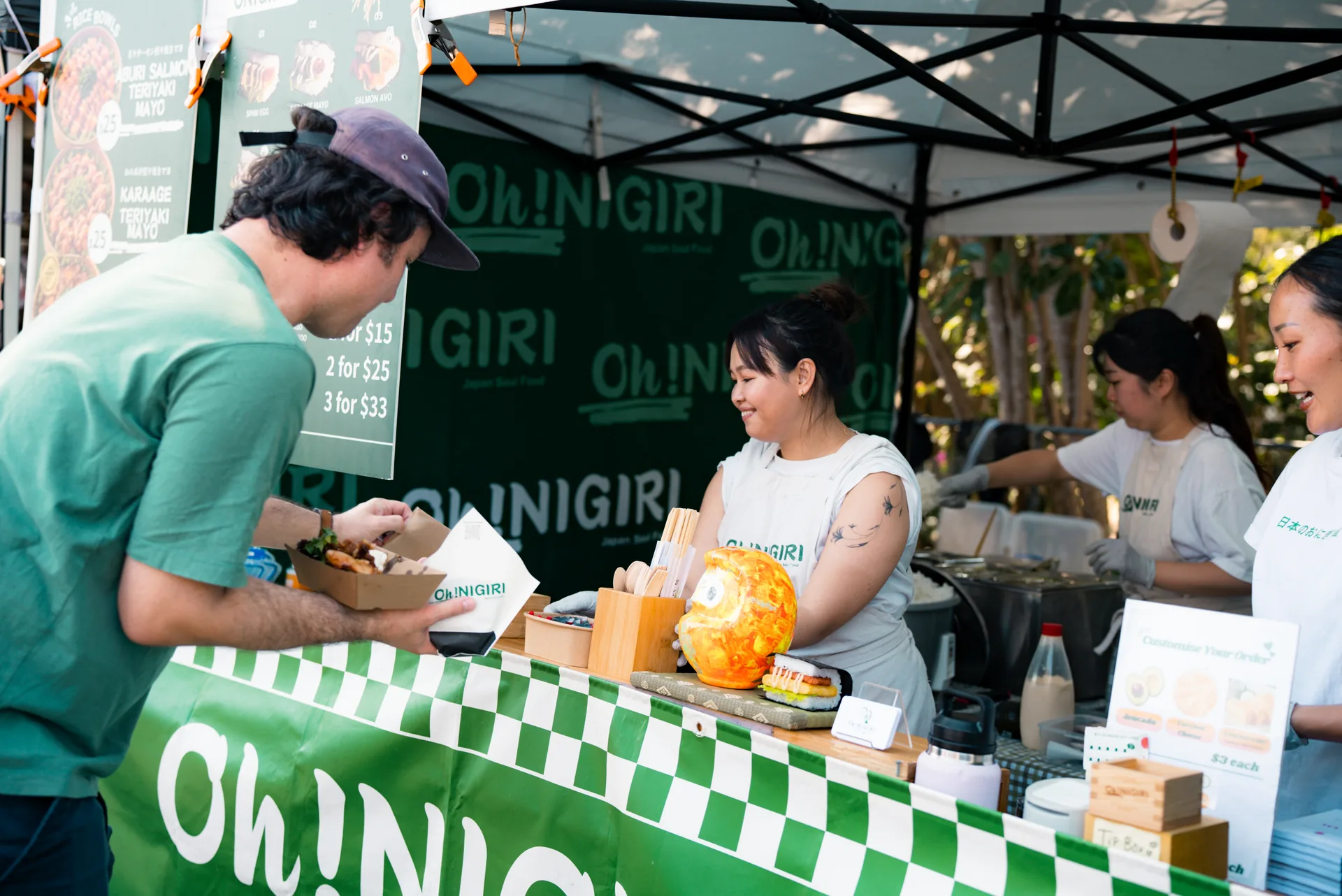Oh!NIGIRI team handing an order to a customer at the market counter